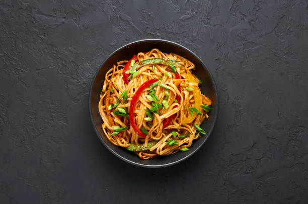 Hakka noodles with peppers and spring onion in a black bowl